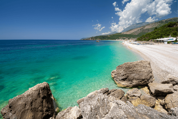 Prodnata plaža Llaman blizu Himare v Albaniji, stisnjena v majhen zaliv med zelenimi griči.
