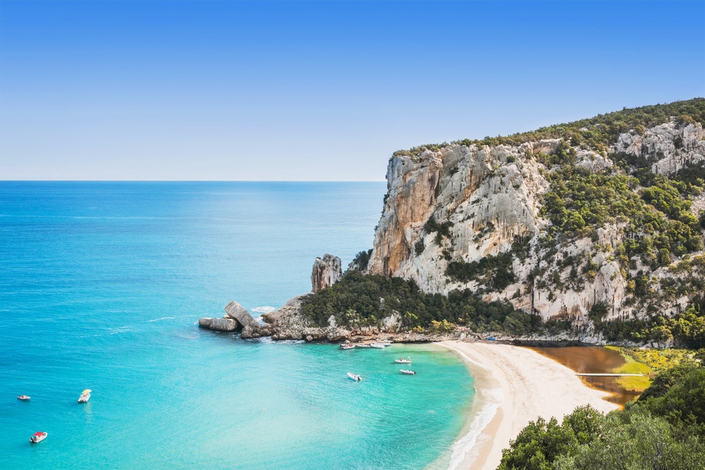 Cala Luna na Sardiniji z belim peskom, modrim morjem in značilnimi jamami ob plaži